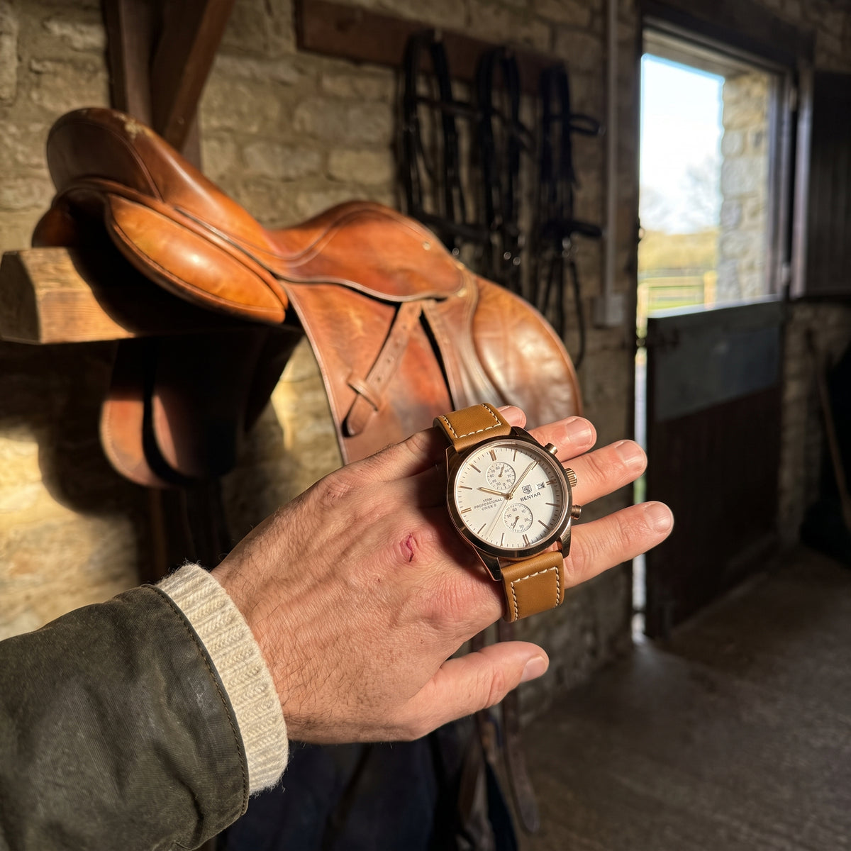 Livorno watch with rose gold-tone case, ivory dial and brown leather strap held in a hand in a stable