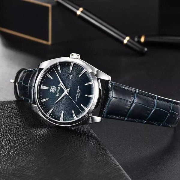 Lucca watch in deep blue and navy leather lying on dark fabric next to a black fountain pen