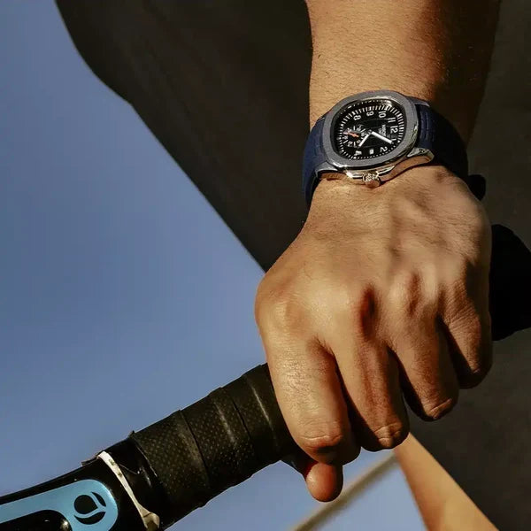 Steel sport watch with dark dial and navy strap worn on the wrist, hand on a bicycle handlebar