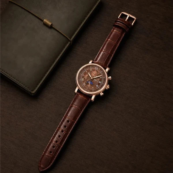 Galileo rose gold-tone watch lying flat beside a leather notebook, showing the full croc-embossed brown strap and pin buckle