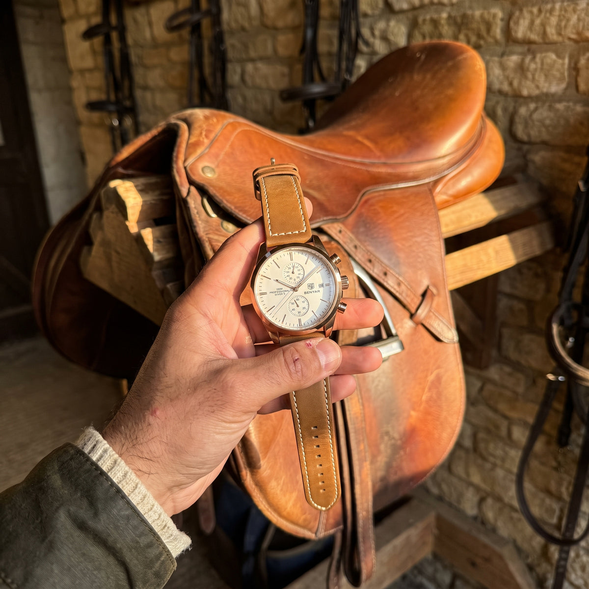 Livorno with rose gold-tone case, ivory dial and brown leather strap held in a hand beside a leather saddle