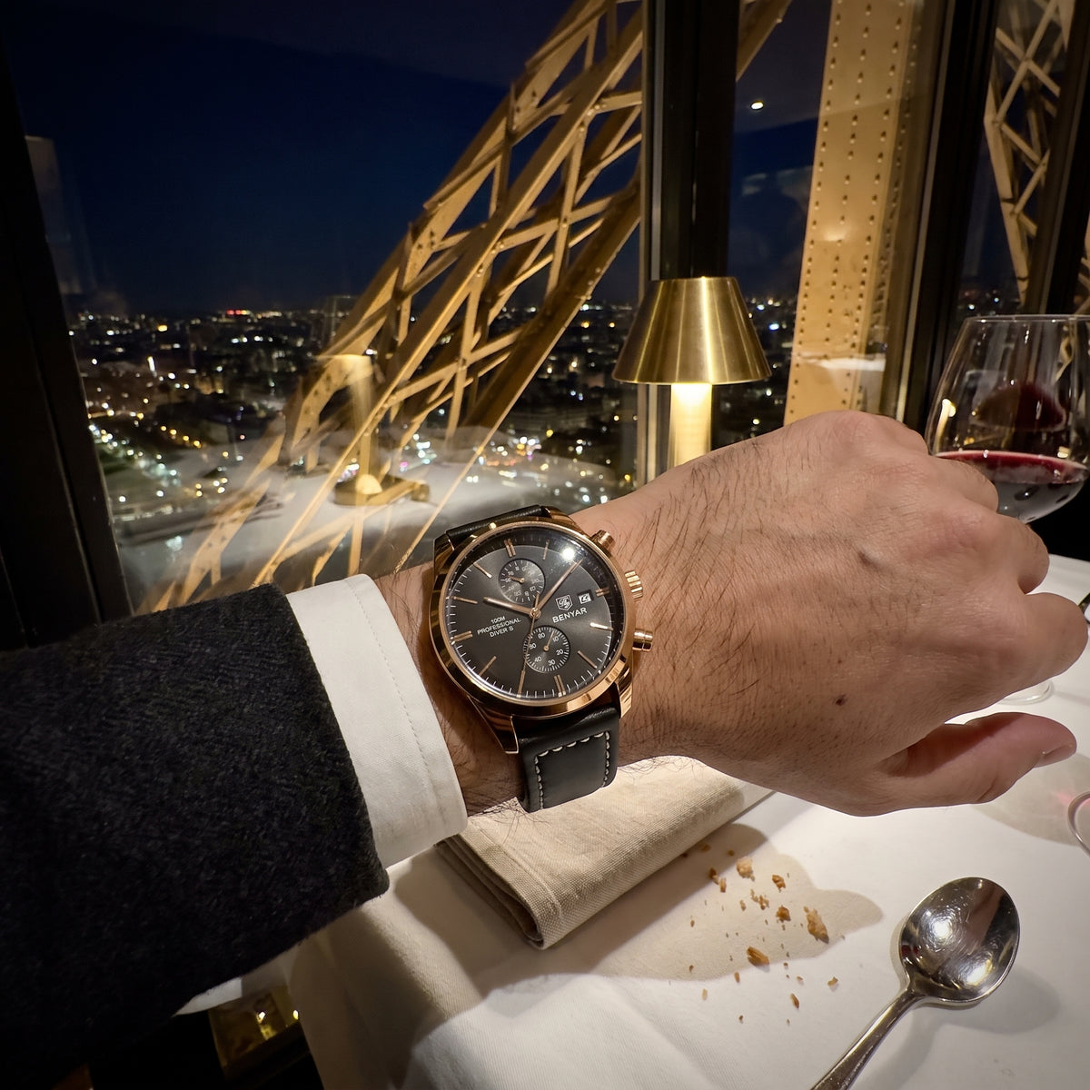 Livorno with rose gold-tone case worn at a dinner table at night with a glass of red wine, city lights behind